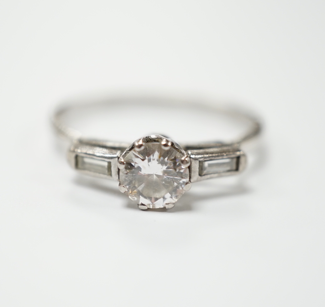 A white metal and single stone diamond set ring, with two stone baguette cut diamond set shoulders, size O, gross weight 2.3 grams, stone diameter 5.2mm.